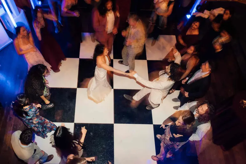 Guests dancing on a black and white checkered dance floor under colored lights, seen from above