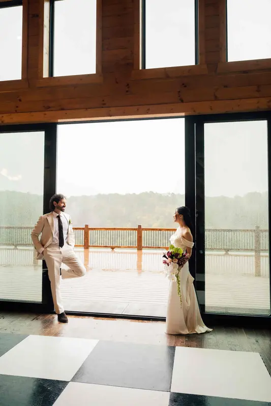 Groom and bride facing each other through the open glass doors of the great room, the deck and gorge beyond
