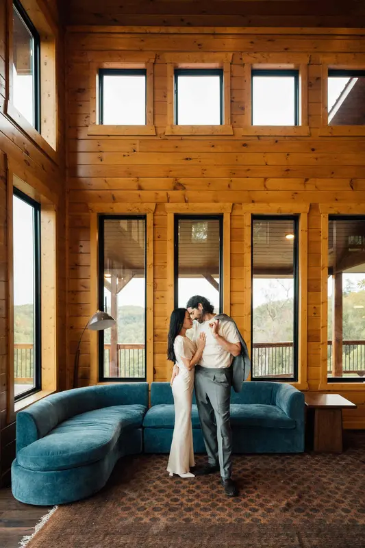 Ji and Noah embracing in the great room beneath the tall windows and wood walls