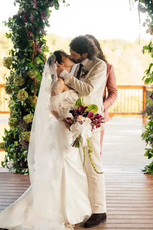 Bride and groom kissing beside the floral arch on the deck, her veil falling to the boards
