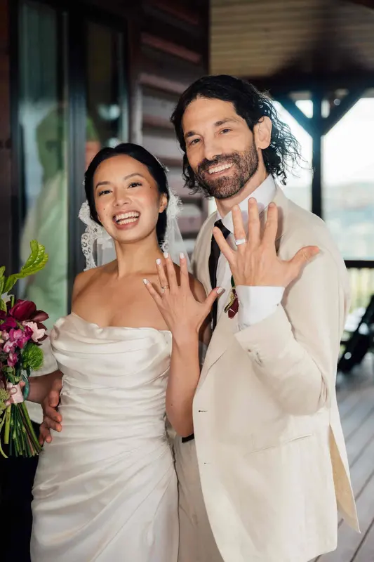 Ji and Noah laughing and showing their wedding rings on the covered porch
