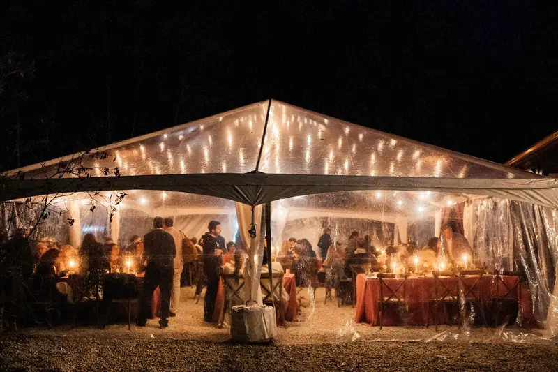A clear-top reception tent glowing with string lights at night, guests inside