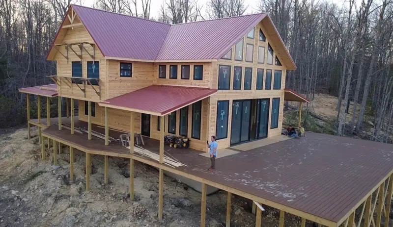 Aerial view of Red River Château's glass gable, red roof and large deck at the forest edge
