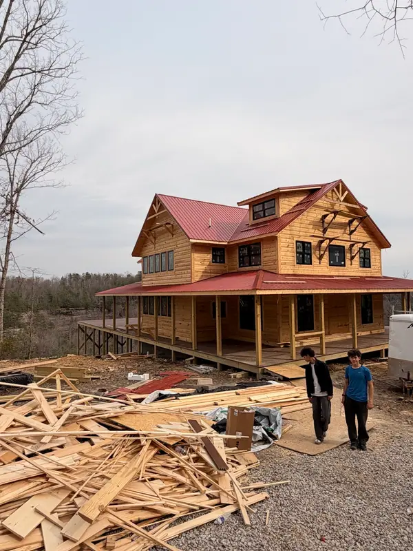Two people walking past lumber toward Red River Château during construction