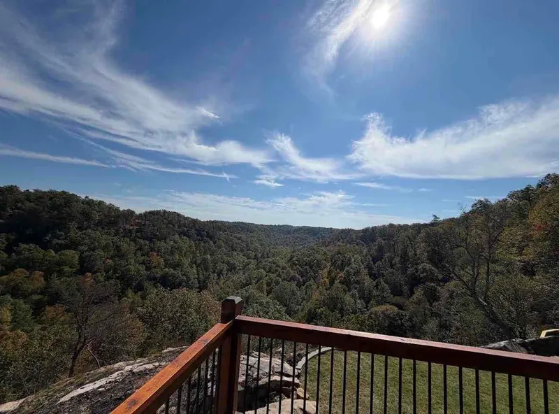 Wide view from the deck railing over a forested gorge under a bright blue sky with wispy clouds