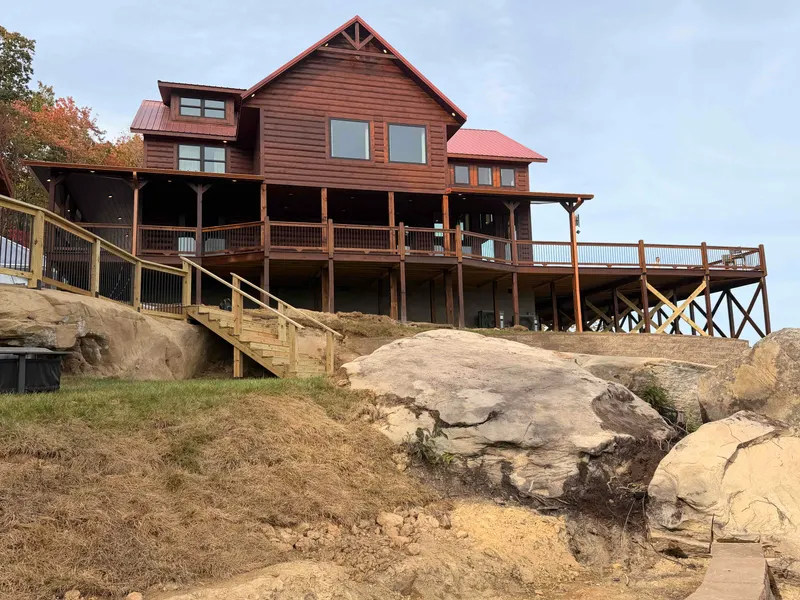 Red River Château's two levels of decks seen from below, above large sandstone boulders and a stairway to the lawn
