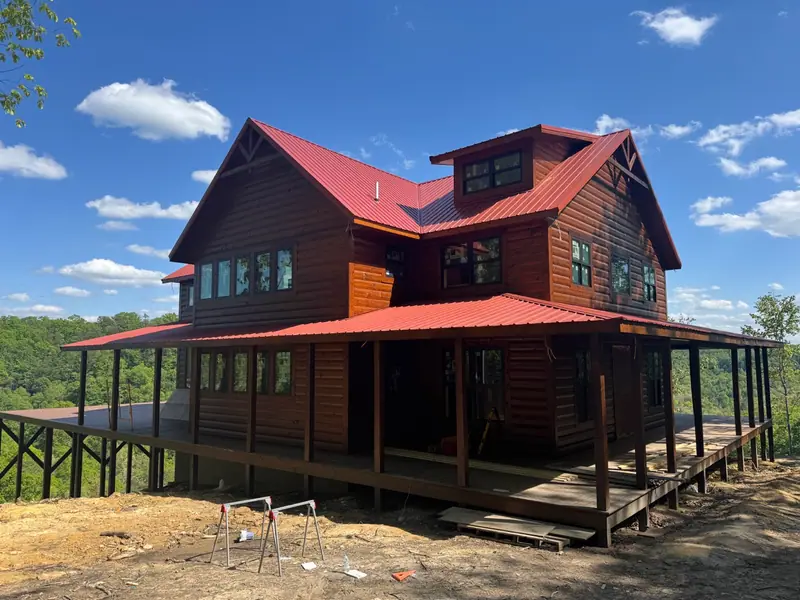 Red River Château's dark-stained wood exterior, red metal roof and wraparound covered porch under a blue sky