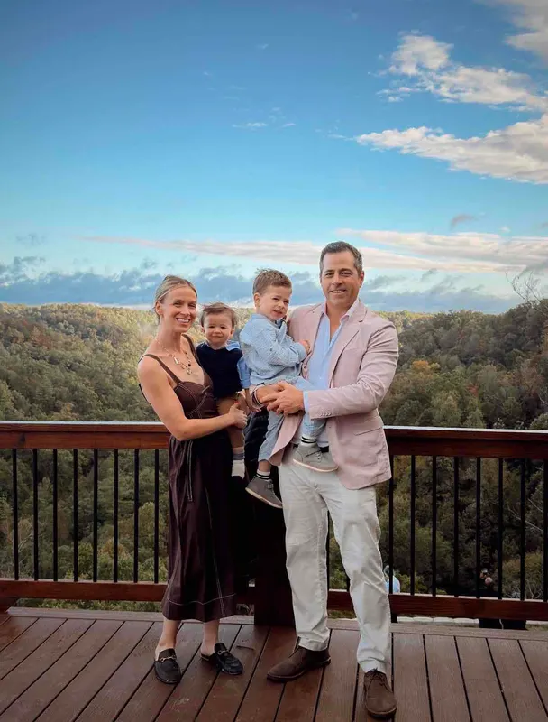 A family with two young children on the deck, with the forested gorge and blue sky behind them