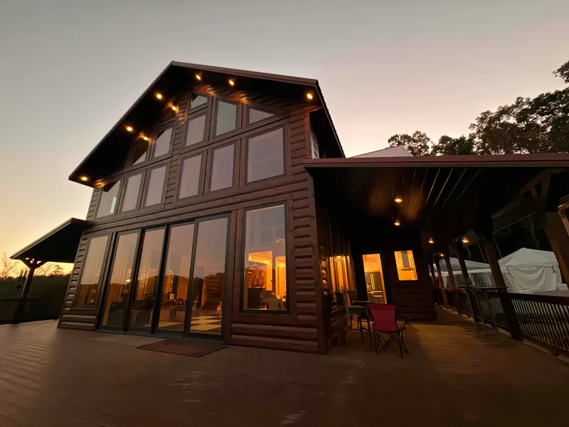 Red River Château at dusk, its glass gable and covered porch lit up above a wide deck