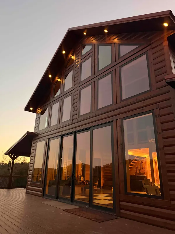 Looking up at Red River Château's two-story glass gable and sliding doors at sunset, with soffit lights glowing