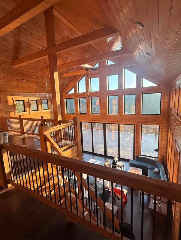 Great room seen from the loft: a vaulted wood ceiling with beams, a wall of windows and the living area below
