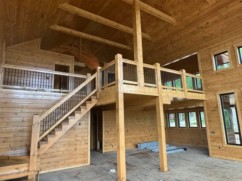 Great room during construction with tongue-and-groove wood walls, a vaulted ceiling, open staircase and loft balcony
