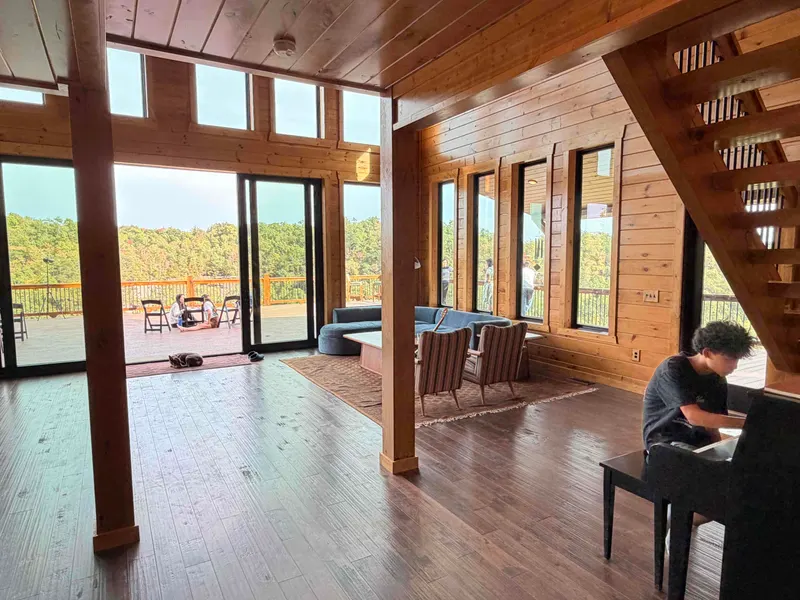 Great room with wood walls, sofas, a piano under the staircase and glass doors opening onto the deck