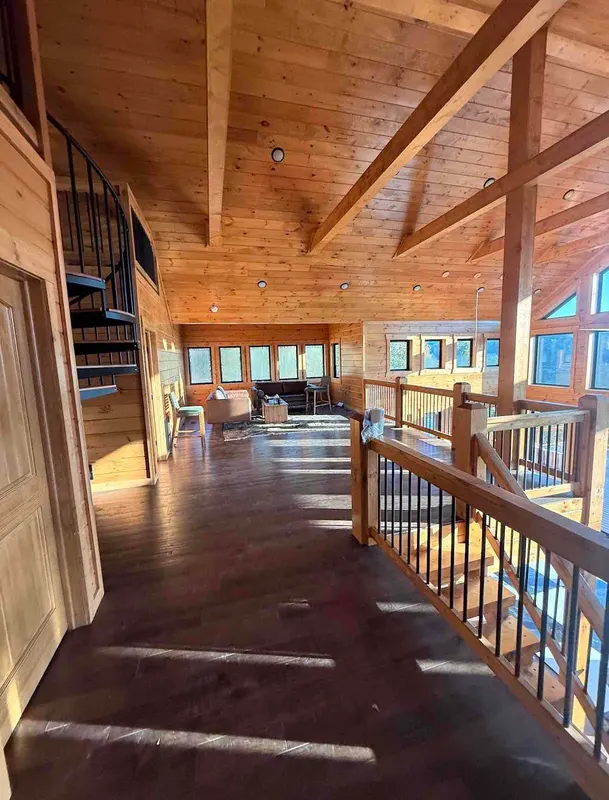Sunlit loft with wood plank walls and ceiling, a seating area under a row of windows and a railing over the great room