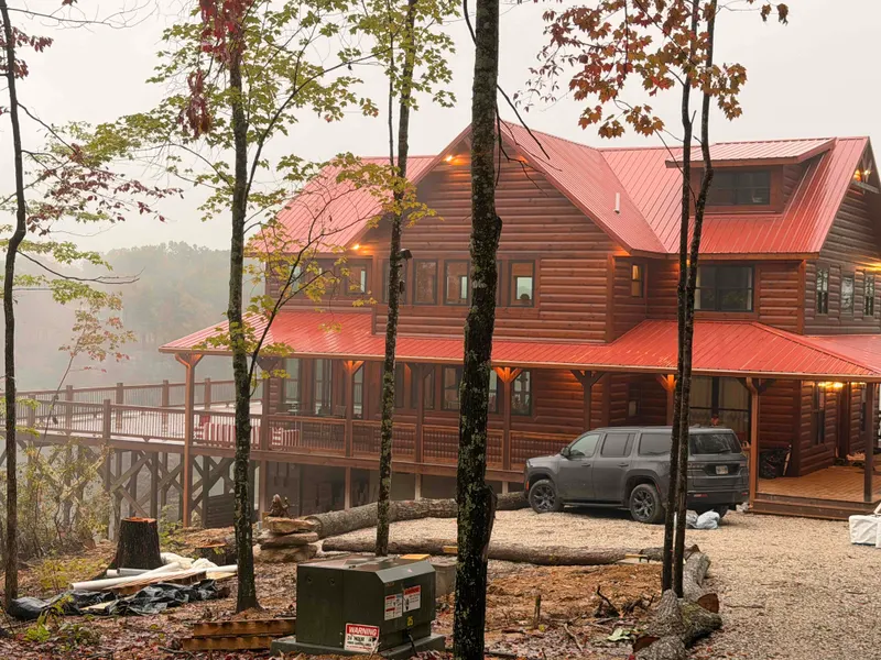 Front of Red River Château with its red metal roof, wraparound porch and elevated deck among fall trees