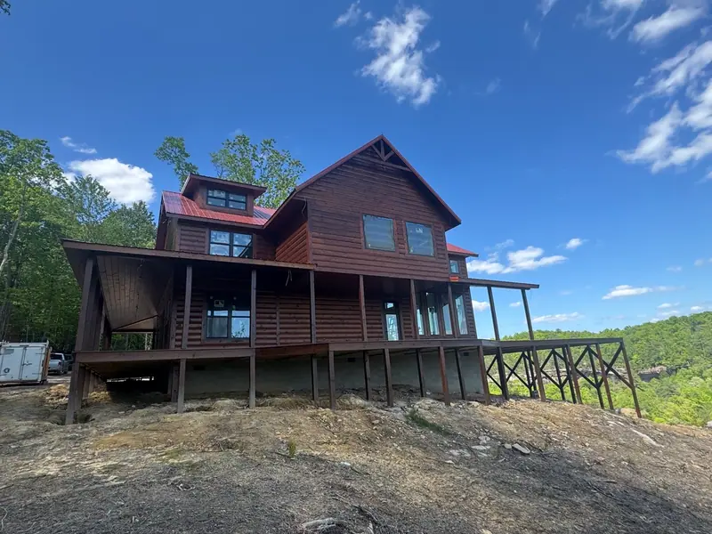 Side view of Red River Château showing the covered porch, dormer windows and forested hills beyond