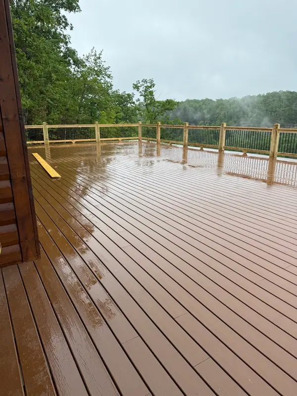 Rain-glossed composite deck with a wooden railing overlooking green treetops and mist